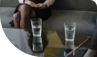 Two people sitting in a room with a coffee table and glasses of water